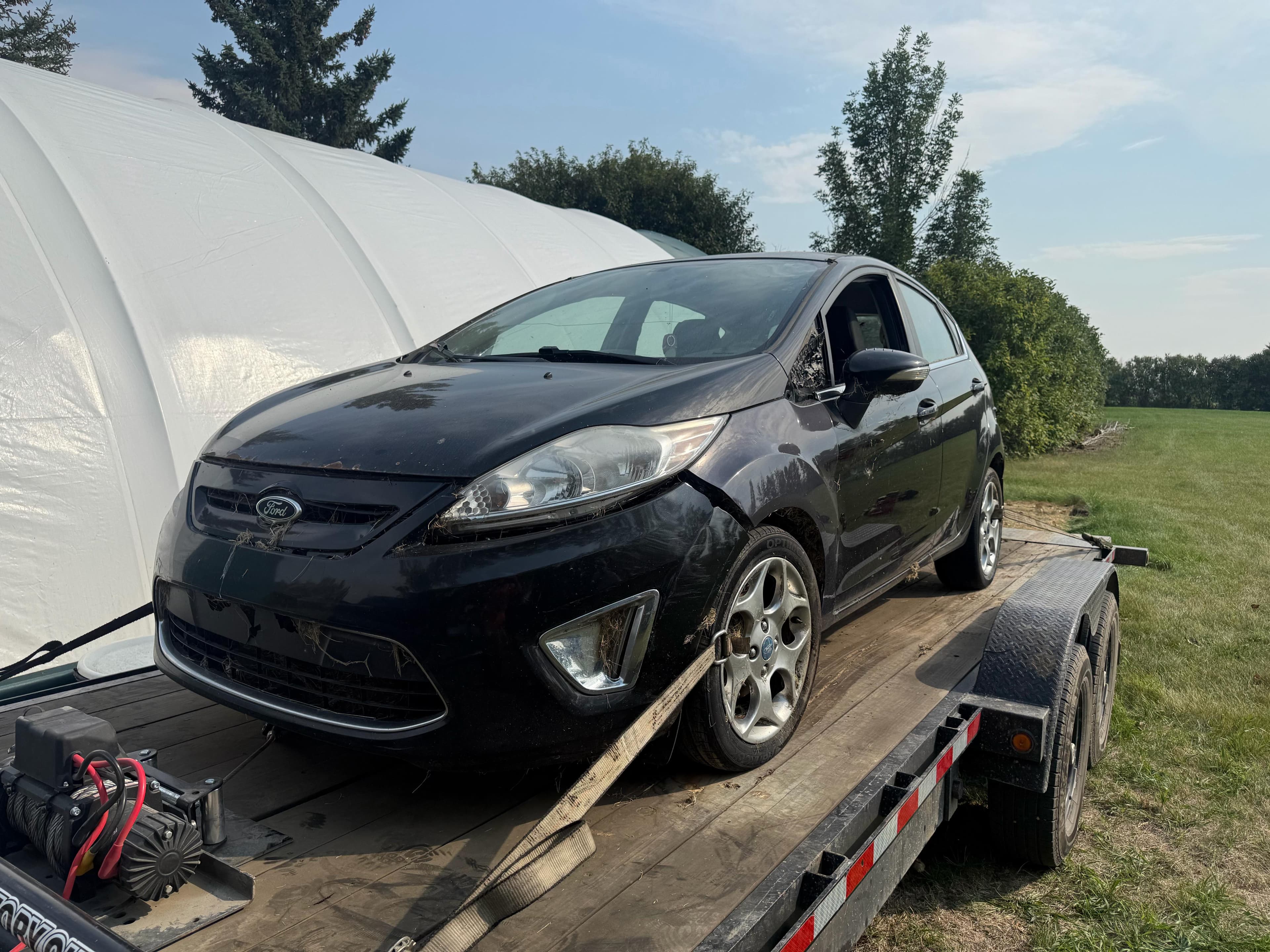 Damaged black Ford Fiesta secured on a trailer for pickup